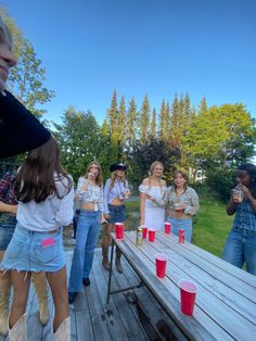 a group of people standing around a picnic table with red cups on it and one person holding a cell phone