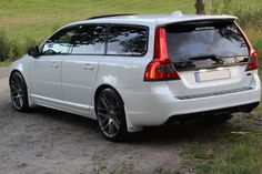 the back end of a white volvo wagon parked on a dirt road next to grass and trees