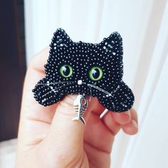 a black cat brooch with green eyes is being held by someone's hand