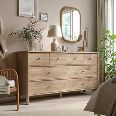 a bedroom scene with focus on the dresser and bed sideboard, mirror and plants