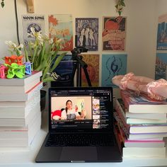 an open laptop computer sitting on top of a desk next to books and vases