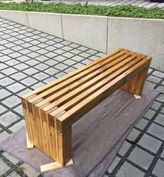 a wooden bench sitting on top of a cement slab next to a wall and grass