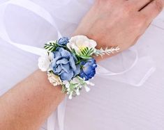 a bride's wrist is adorned with blue and white flowers