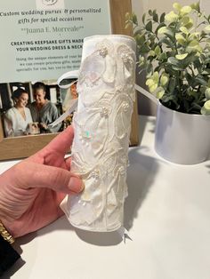 a hand holding a white vase on top of a table next to a flower pot