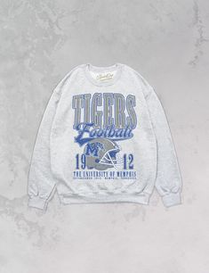 **Officially licensed with the University of Memphis** Show the love for your favorite team in our one and only Memphis Tigers Football oversized 90's sweatshirt. - Features Tigers Football with a helmet featuring the official Tigers logo with 1912 beside it and The University of Memphis, Established 1912. Memphis Tennessee underneath all in a blue, gray and white ink - Heat print transfer that is heat pressed onto each sweatshirt- Printed on a soft, 90's style oversized crewneck sweatshirt- Cot Style Oversized Crewneck, Memphis Tigers Football, University Of Memphis, 90s Sports, Memphis Tigers, Tiger Football, Tiger Logo, 90s Sweatshirt, Print Transfer