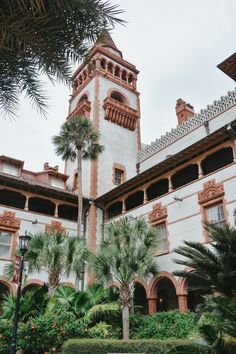 a tall building with a clock tower next to palm trees and other greenery in front of it