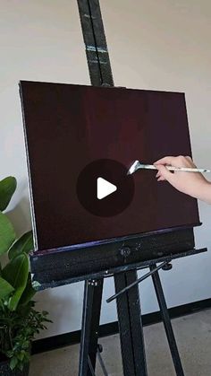 a woman is painting on an easel with a paintbrush in front of her