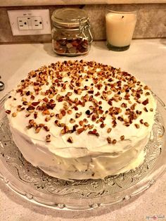 a cake with white frosting and nuts on top sitting on a glass platter