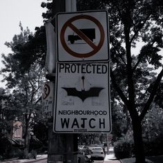 two street signs on a pole with cars parked in the background and trees behind them