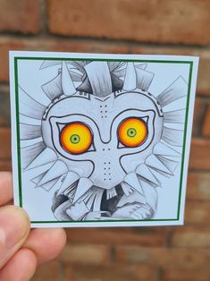 a hand holding up a sticker with an image of a demon's face