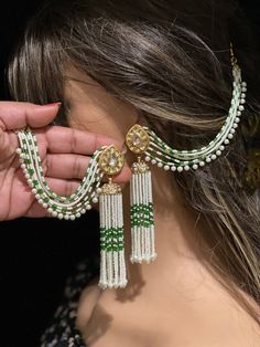 a woman is holding some pearls and green beads on her earring, while she holds the