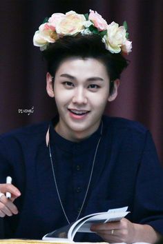 a young man with a flower crown on his head is reading a book and smiling