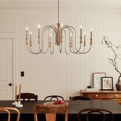 a chandelier hangs over a dining table in a room with white walls and wooden furniture