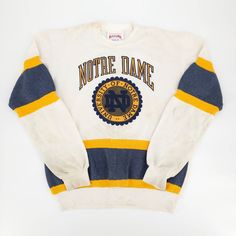 Vintage Notre Dame Fighting Irish Stripe Sweatshirt Brand: Nutmeg Mills Color: White/Yellow/Navy Size: Fits S/M Made In Usa - Vintage 80s - Crewneck - Printed Logo - Rib Knit At Neck, Cuff And Hem - University Of Notre Dame - Ncaa, Sports - Collectible - Stripe Detailing Approx: 20” Armpit To Armpit 23" Length (Shoulder To Hem) 18" Shoulder Seam To Seam 6" Collar To Shoulder Seam 23.5" Sleeve Length Condition: Has Vintage Wear And Discoloration, Please See Pictures For Detail. Sku: Ct-313 Vintage White Sweatshirt For College, White Retro Sweatshirt, Vintage Yellow Crew Neck Sweatshirt, Retro White Sweatshirt With Ribbed Cuffs, Vintage Yellow Long Sleeve Sweatshirt, Yellow Vintage Long Sleeve Sweatshirt, Retro White Sweatshirt For College, Vintage College Sweatshirts, Vintage Notre Dame