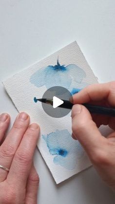 someone is painting flowers with blue watercolors on white paper and using a brush