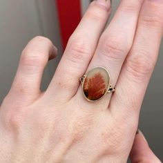 It almost looks like a reef on fire trapped in this Black and Orange Dendrite agate. set in 14k yellow gold bezel with sterling silver back this one of a kind beauty is finished with Emily's 14k gold seagrass band. Approximate stone size: 17mm x 13mm Approx ct weight: 4.4cts Mohs Hardness scale: 7 This one of a kind piece is handmade with love in Emily's Hudson Valley studio. If you have questions about sizing, shipping or need help deciding on your perfect piece please reach out to us! Yellow Gold Agate Ring, 14k Gold Oval Jewelry With Natural Stones, Yellow Gold Oval Agate Jewelry, Oval Agate Gemstone Jewelry, Fine Jewelry In Yellow Gold With Natural Inclusions, Oval Agate Jewelry For Anniversary, Oval Agate Yellow Gold Jewelry, Anniversary Jewelry With Natural Inclusions In Oval Shape, Nature-inspired Jewelry For Anniversary