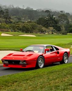 a red sports car driving down a road next to a green field and golf course