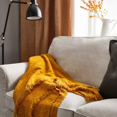 a couch with a blanket on it next to a lamp and flowers in a vase