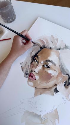 a person is painting a woman's face with watercolors on white paper