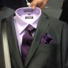 a man in a suit and purple tie is holding his shirt on the hanger