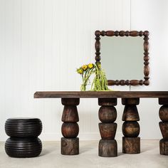 a wooden table sitting next to a mirror on top of a white wall with flowers in it