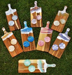 wooden cutting boards with painted paint on them sitting in the grass next to each other