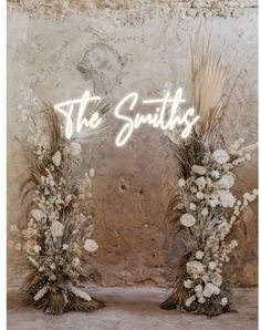 two floral arrangements with the words the smiths in neon lights above them, against a stone wall