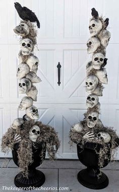 two tall black vases with skulls and feathers on them sitting in front of a garage door