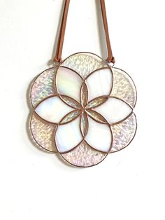 a white and brown flower shaped purse hanging on a wall with leather strap around it