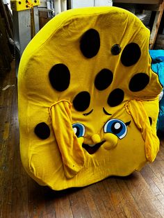 a yellow chair with black spots on it's face and eyes, sitting in a room