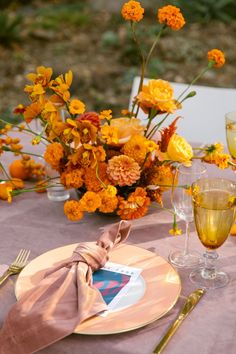 the table is set with yellow and orange flowers in vases, wine glasses, and napkins