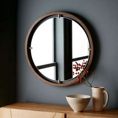 a round mirror hanging on the side of a wall next to a vase with flowers