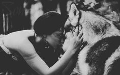 a woman kissing a wolf on the nose in black and white photo with trees behind her