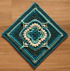 a crocheted square is shown on a wooden surface, with white and blue accents