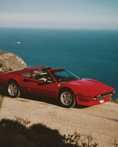 a red sports car parked on the side of a road next to the ocean in front of a cliff