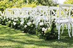 rows of white chairs lined up in the grass with flowers on them and greenery