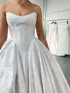 a woman in a white wedding dress standing next to a rack with dresses on it