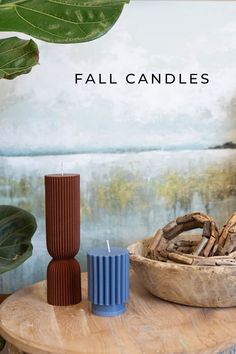 two candles sitting on top of a wooden table next to a basket filled with leaves