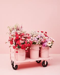 three pink flower pots sitting on top of a wooden cart with flowers in each one