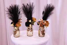 three vases filled with flowers and feathers on top of a white table cloth covered backdrop