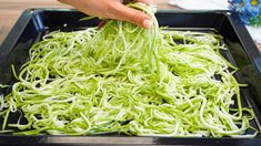 someone is sprinkling green noodles on a tray