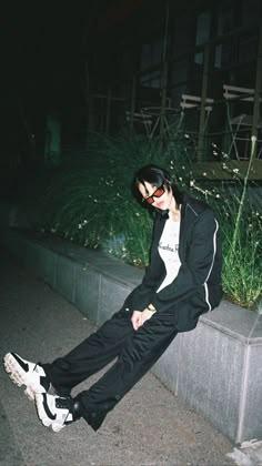 a young man sitting on the side of a cement wall next to a planter