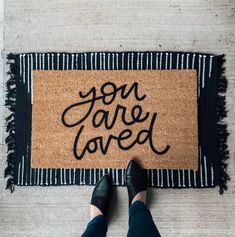 someone standing in front of a door mat that says you are loved