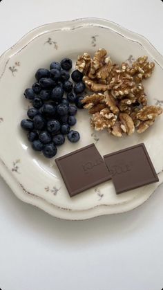 a white plate topped with blueberries and walnuts next to a bar of chocolate