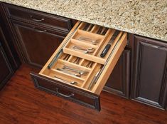 an open drawer with utensils in it on a wooden floor next to black cabinets