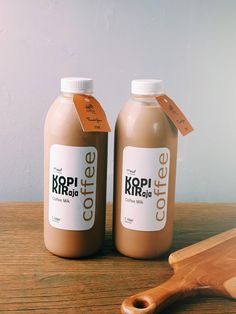 two bottles of coffee sitting on top of a wooden table next to a cutting board