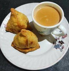 two pastries on a plate next to a cup of coffee with saucer and spoon