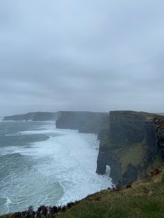 an ocean view with waves crashing on the shore and cliffs in the distance, under a cloudy sky