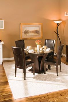 a dinning room table and chairs in front of a painting on the wall with candles