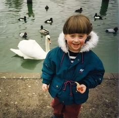 a young boy is standing in front of some ducks and swans on the water's edge